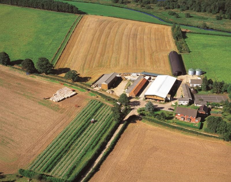 An aerial view of farmland, farm buildings, harvested fields and a river running through the fields.