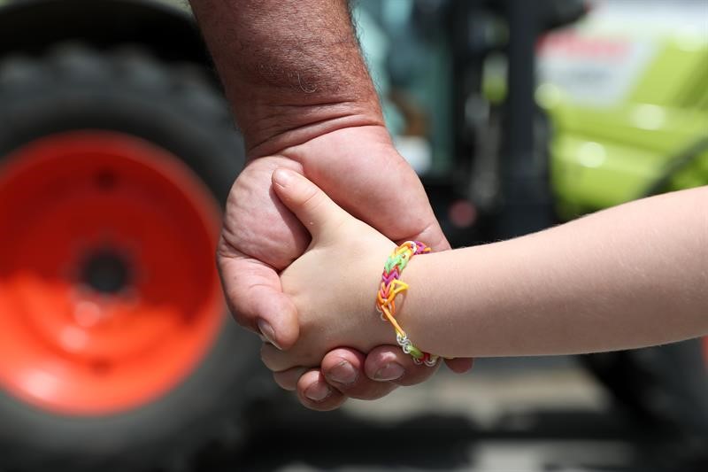 Farmer holding a child's hand in front of a tractor