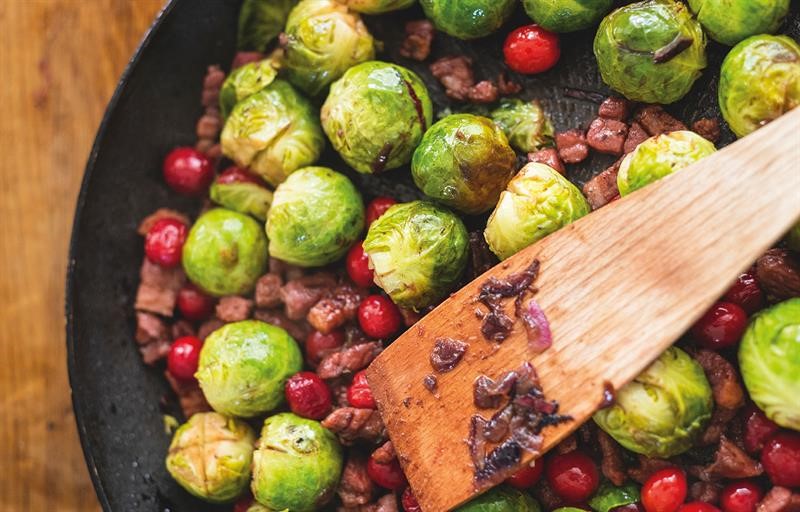 Sprouts cooked with bacon and cranberries in a dish with a wooden spoon.