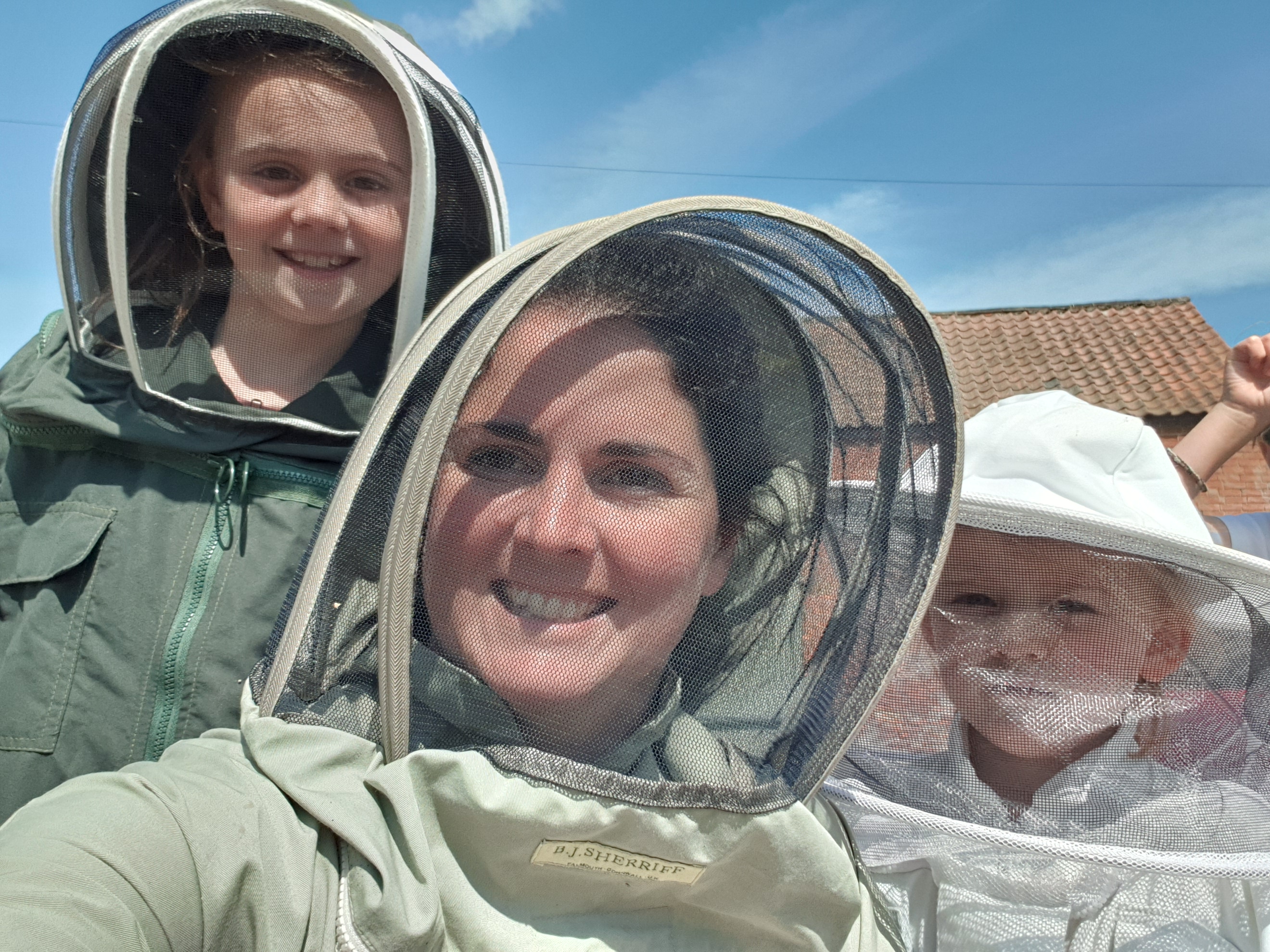 An image of a woman and two children wearing bee keeper uniforms