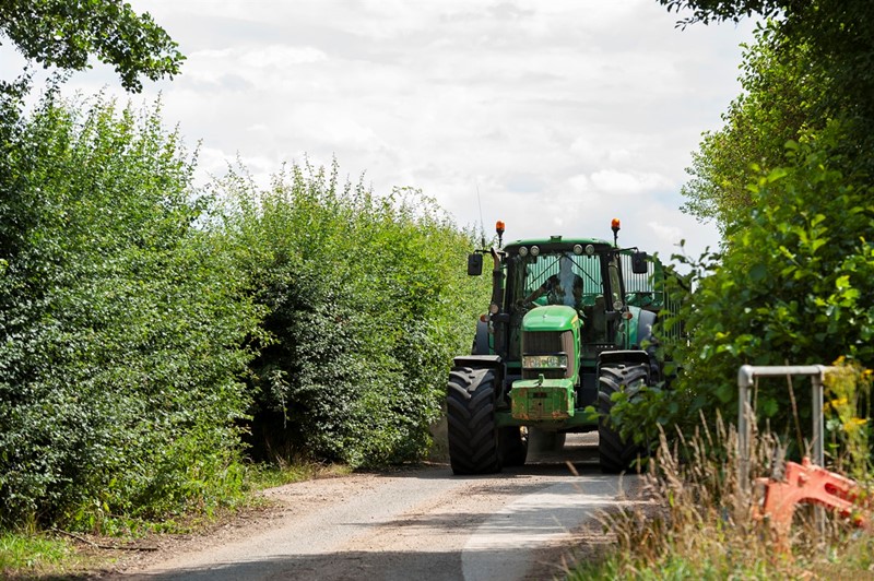 A picture of a tractor on a narrow lane with high hedges either side of the road