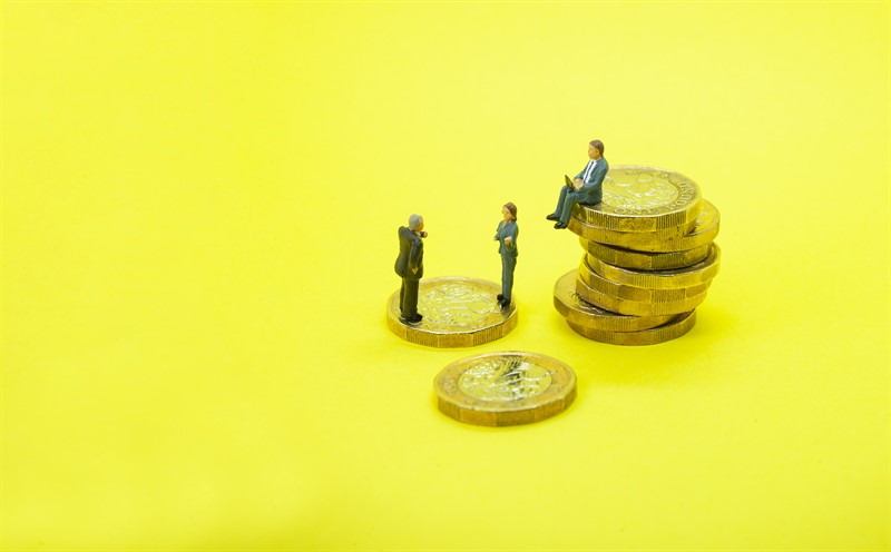 Three miniature figures of business people with one sitting on a pile of pound coins