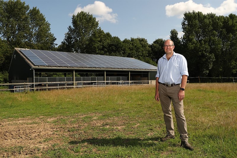 Image of NFU Deputy President Tom Bradshaw in a field with solar panels on the rooftop of a barn behind him.