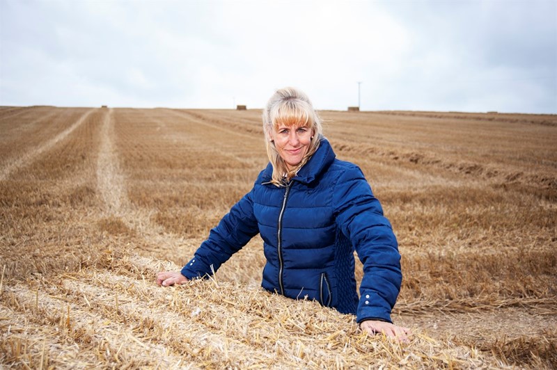 NFU President Minette Batters leaning against a bale of straw in a field.