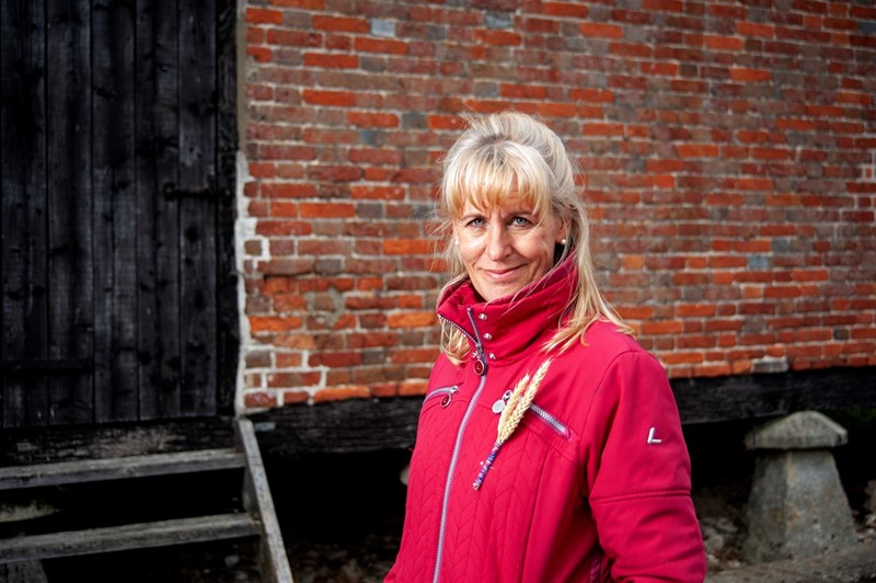 NFU President Minette Batters in front of a barn wearing the Back British Farming Day wheatsheaf pin badge, smiling.