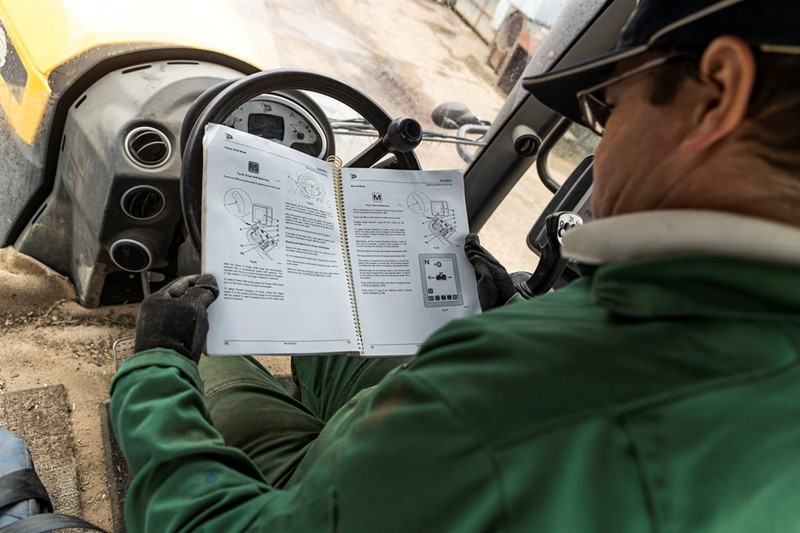 A picture of a male farmer reading an instruction manual in a tractor