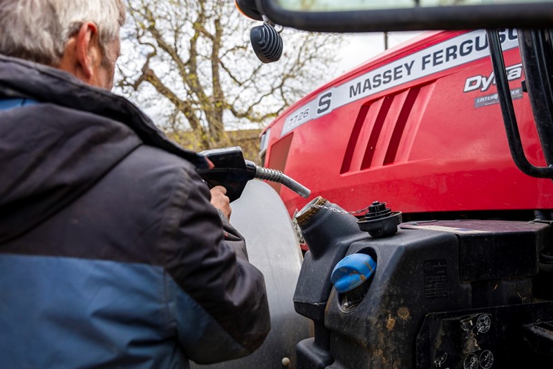  A picture of a man holding a diesel pump nozzle putting fuel into a tractor fuel tank