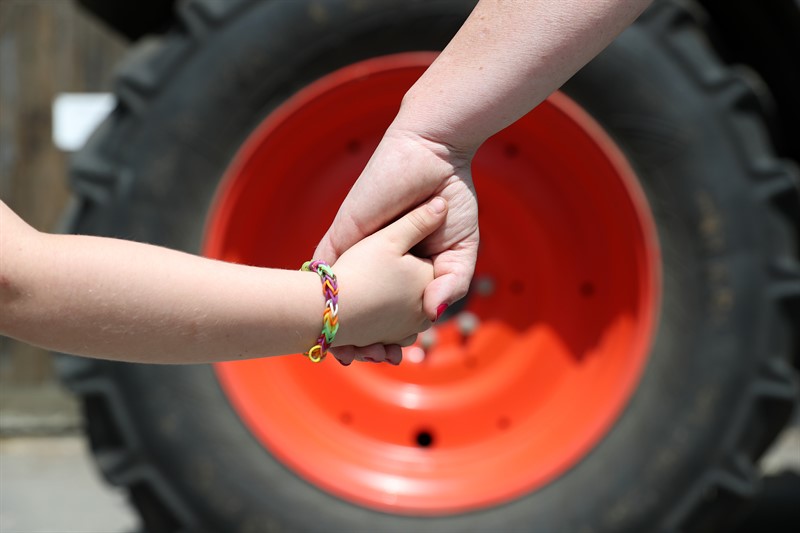 A child's hand holding an adult's hand with a tractor tyre in the background