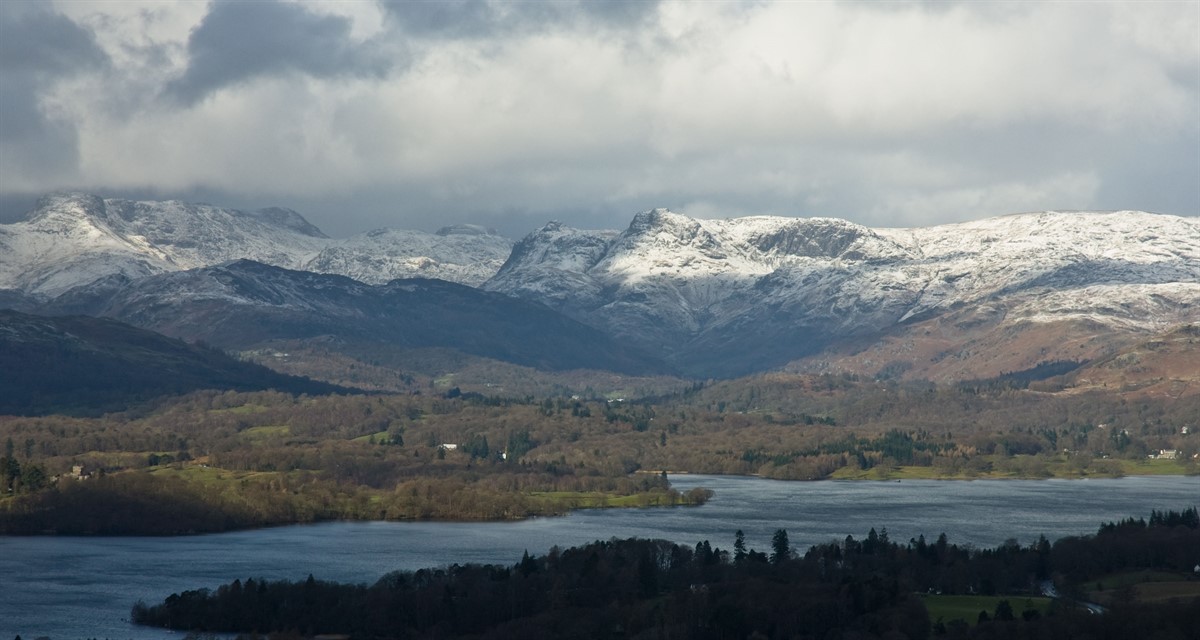A photo of Lake Windermere in Cumbria with a snowy mountain landscape background