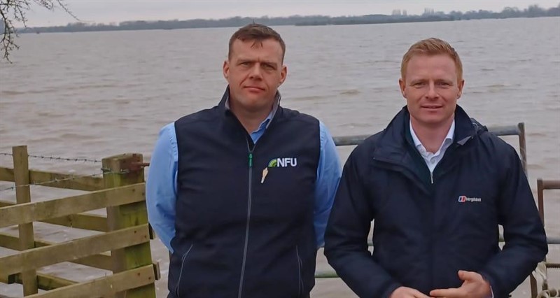 A photo of James Copeland with Robbie Moore MP stood in front of a gate with flooded farmland behind them