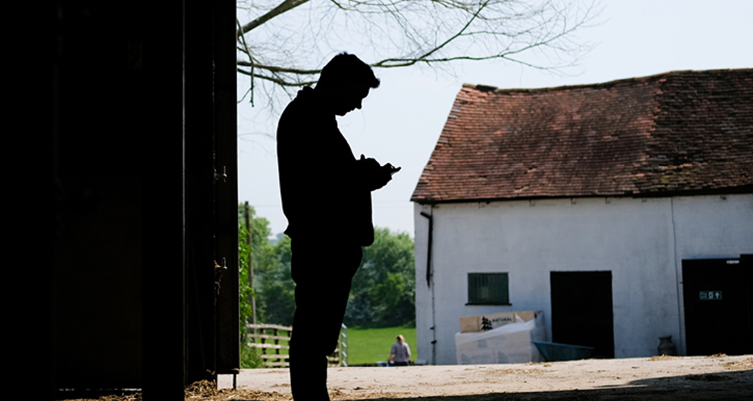 An image of a farmer in a farming building looking at their phone