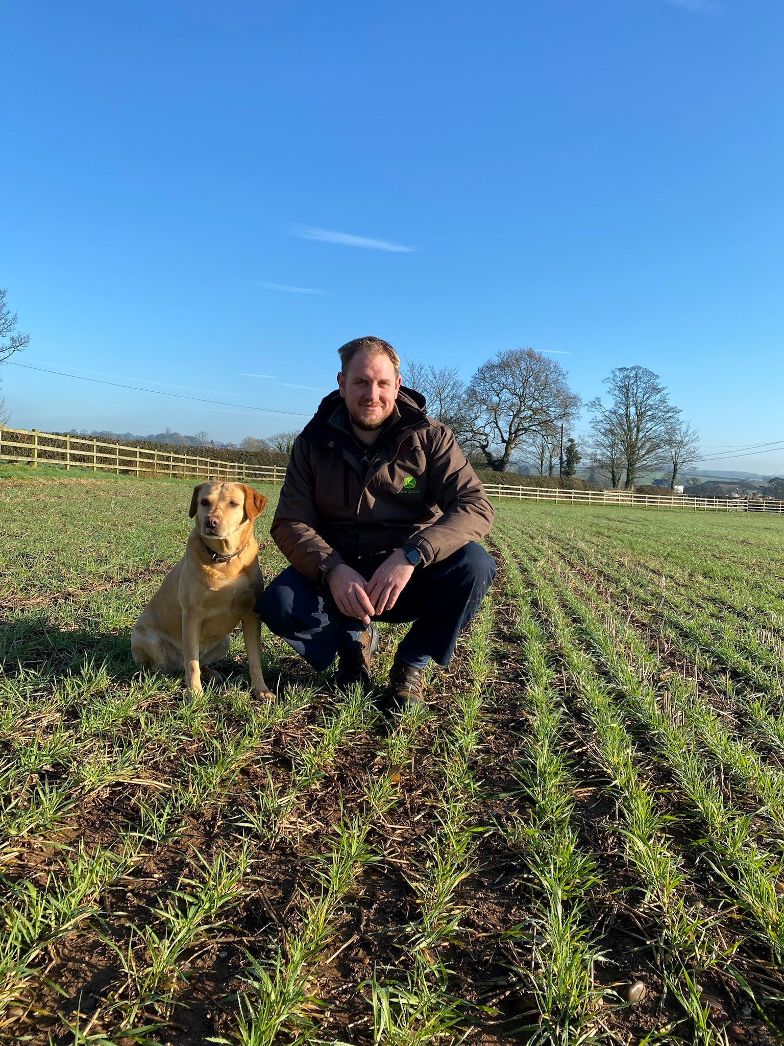 A picture of Rob Atkin crouched down in a field with his yellow labrador.