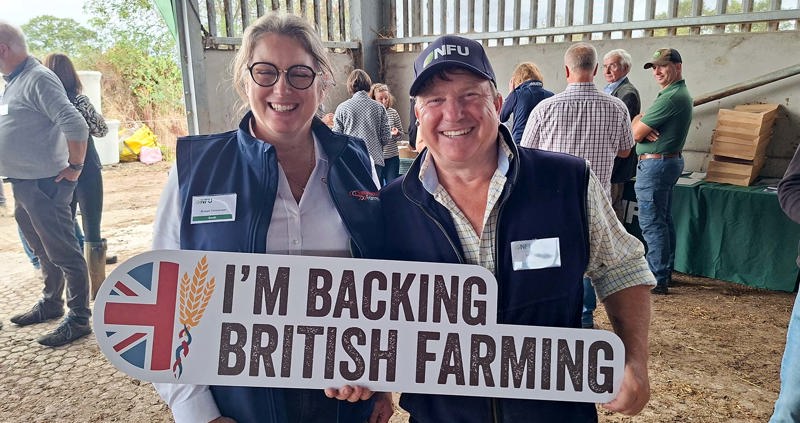 Two people in a barn holding a Back British Farming sign