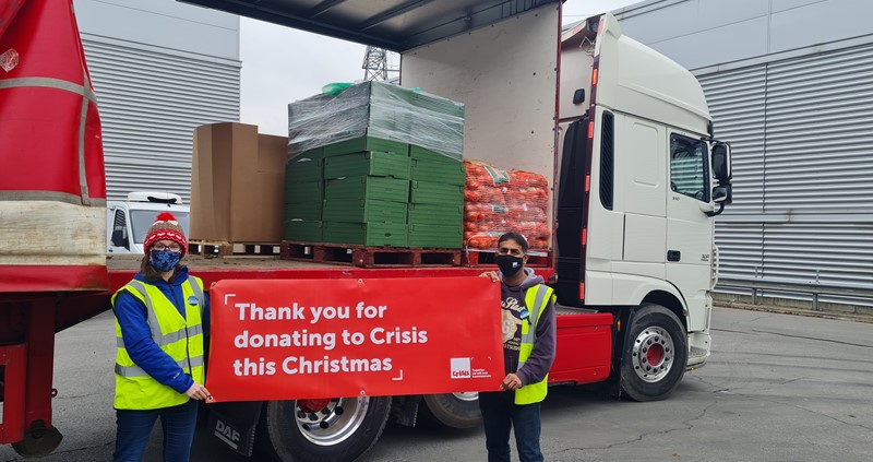 Two people stood in front of a lorry holding a sign saying 'Thank you for donating to Crisis this Christmas'