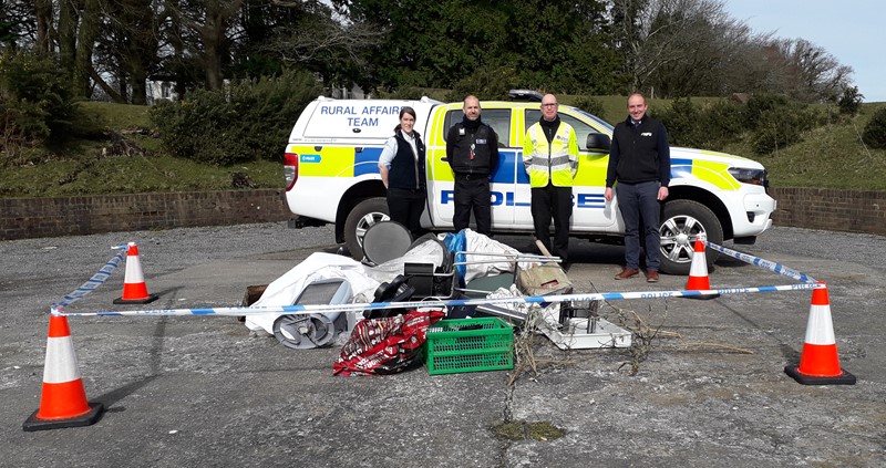 People standing by a police car behind a fake 'fly tip'