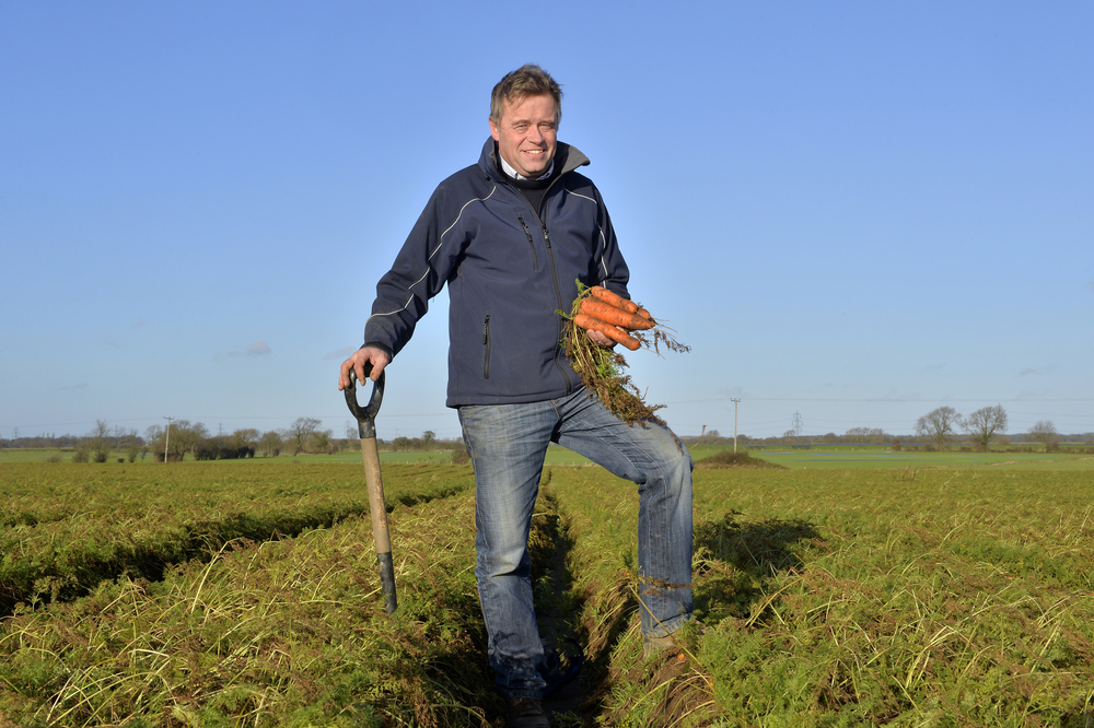 Guy Poskitt, on his farm in Yorkshire, holding a bunch of carrots, leaning on a fork