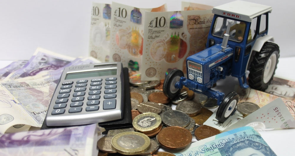 A pile of cash with a miniature tractor and calculator