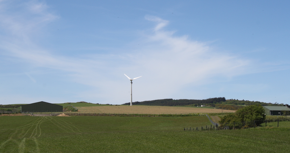 A field a barn and a lone wind turbine