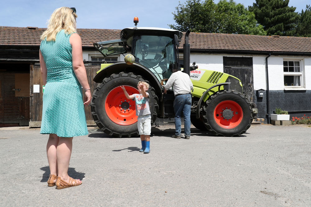 Child playing on farm courtyard while mother watches on and father works in background