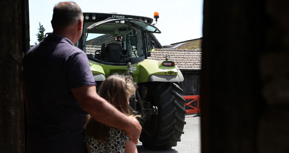 Farmer with his arm around a child while watching a tractor work