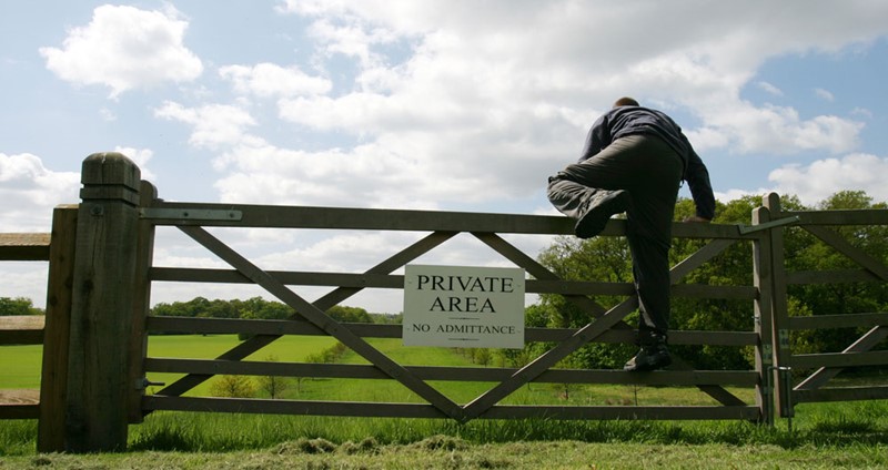 Man climbing over farm gate with a ‘Private area no admitance’ sign