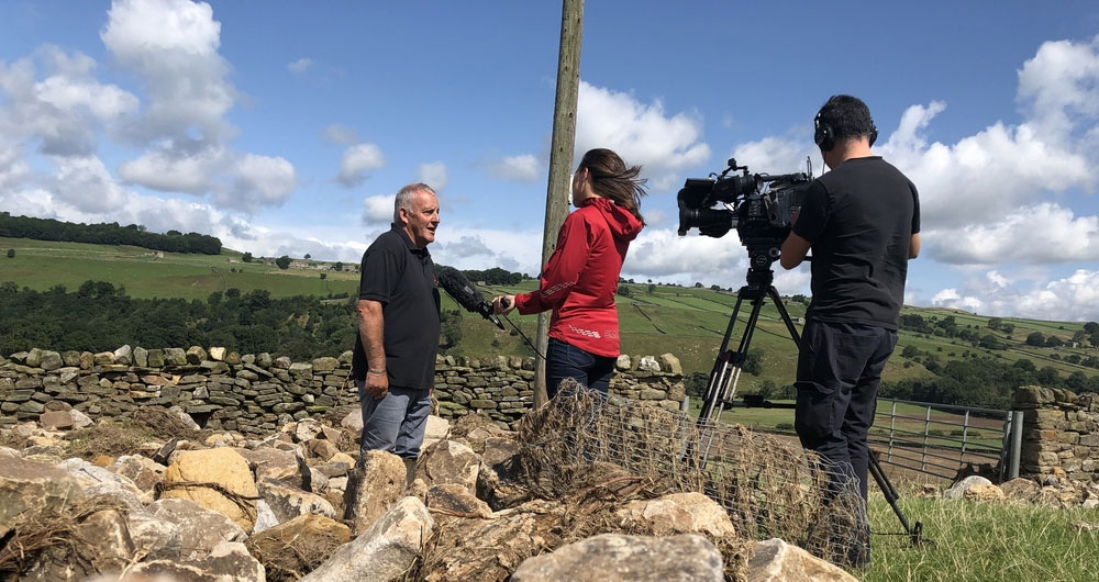 Dales farmer Mike Barker being interviewed by BBC Look North surrounded by stone deposited on his fields by the floods