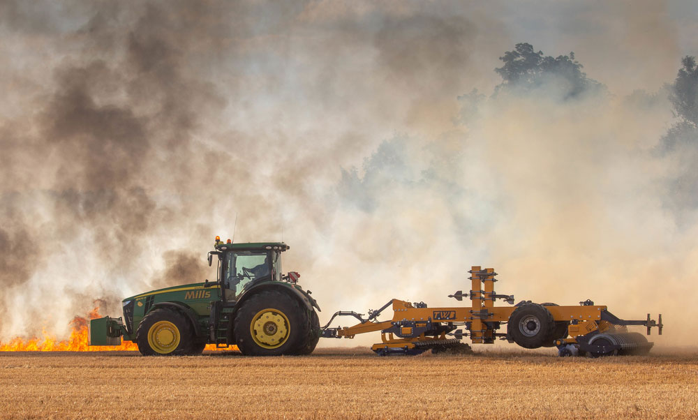 A picture of a tractor pulling a combine with fire blazing in a field of harvested crops